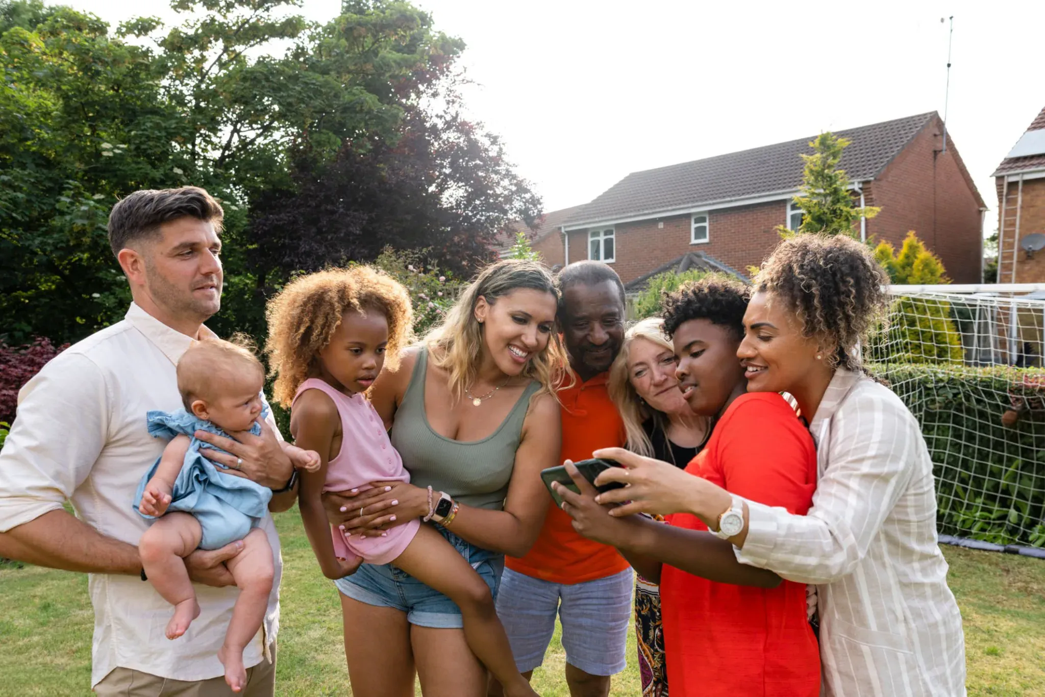 A multigenerational, multiethnic family gathered around a phone in their neighborhood